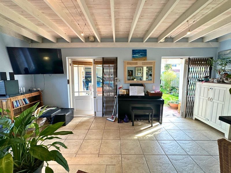 Living room featuring exposed beam ceilings, ceramic floor tiles, and dual access points to the garden through security-gated glass doors.