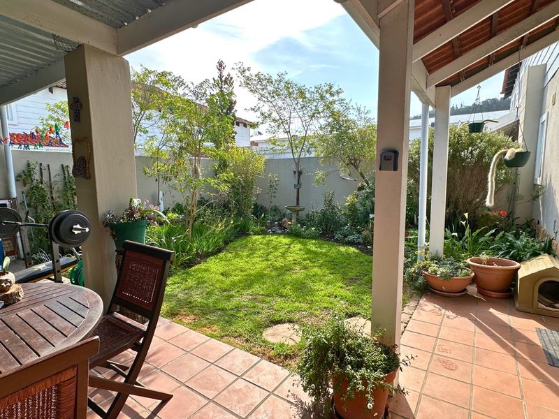 A covered patio area with tiled flooring, overlooking a private garden with a lawn and boundary wall.