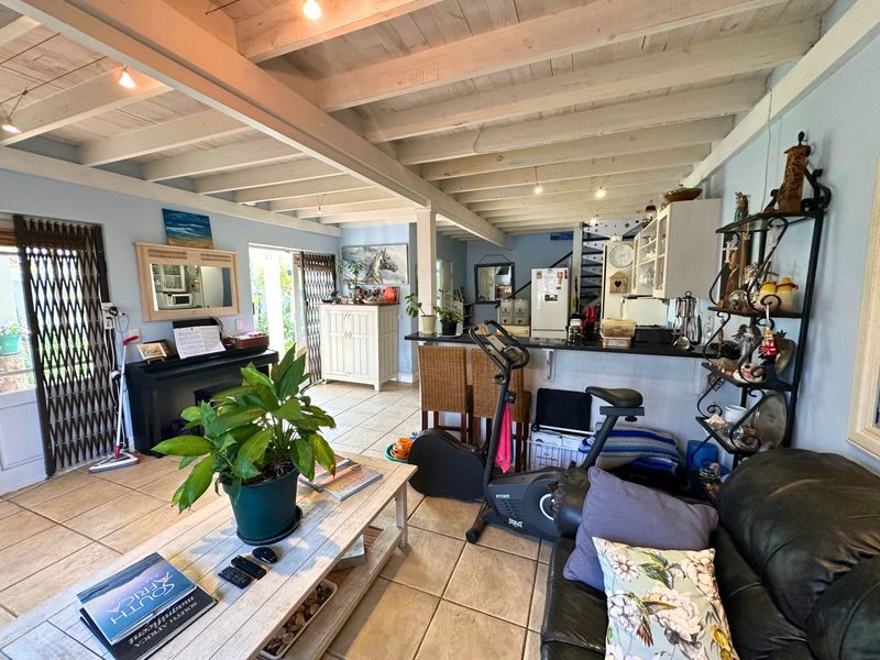 Open-plan living area featuring exposed timber beam ceilings, ceramic tiled flooring, a breakfast bar, and a spiral staircase leading to the upper level.