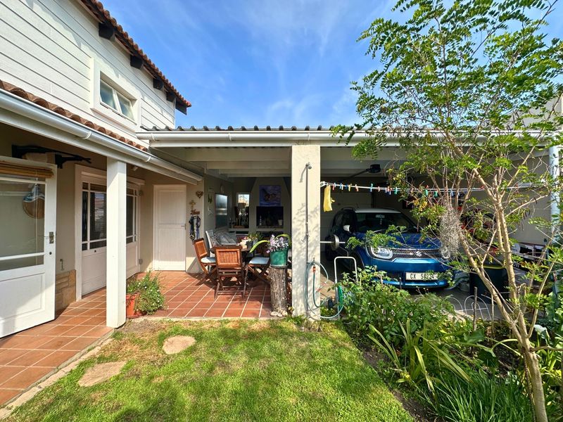 Rear view of the property featuring a covered patio with built-in braai, adjacent garage, and a well-maintained garden area.