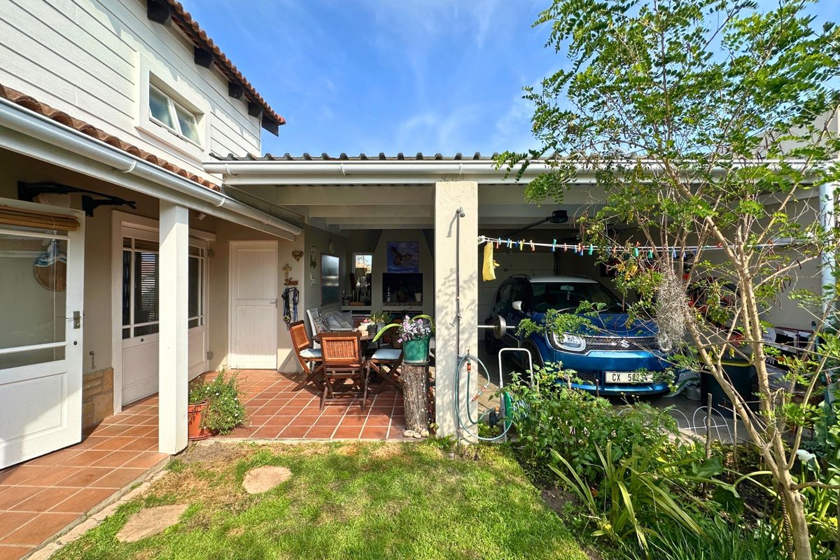 Rear view of the property featuring a covered patio with built-in braai, adjacent garage, and a well-maintained garden area.