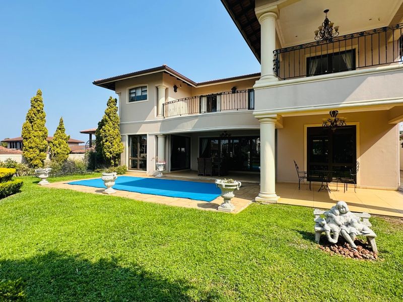 Rear view of a two-story residence featuring a covered patio, upper balcony with wrought iron railings, and a swimming pool set in a landscaped garden.