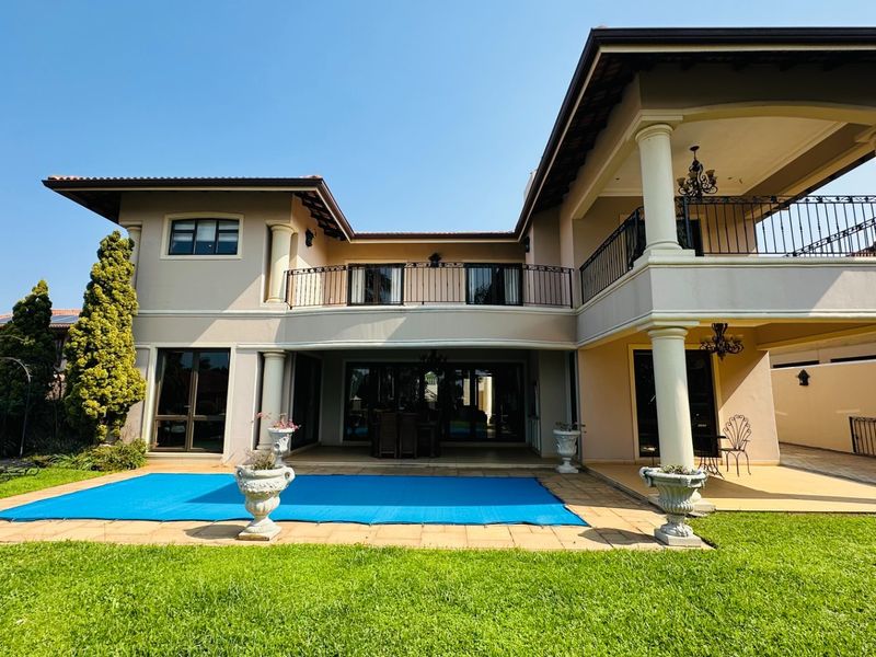Rear view of a two-story residence featuring a swimming pool, covered patio, and an upper-level balcony with wrought iron railings.