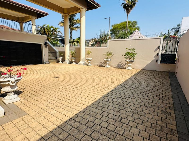 A spacious paved front driveway featuring structural columns, a double garage, and secure boundary walls with a gated entrance.