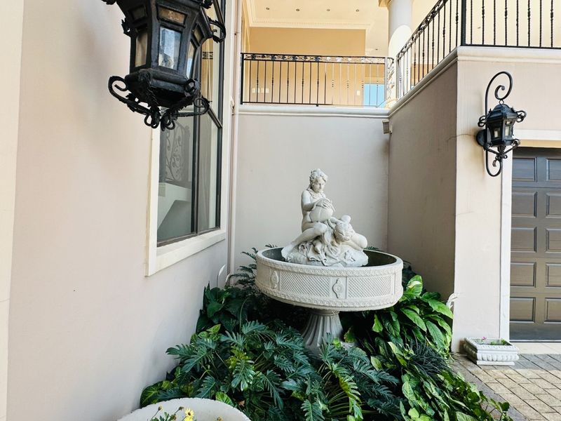 A well-maintained rear courtyard area featuring a decorative stone fountain, wrought iron railings, and access to the garage.