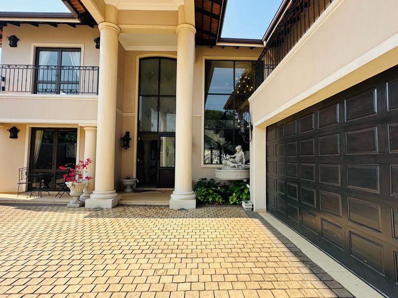 A grand double-storey residence featuring a paved driveway, double garage, covered entrance with classical columns, and elegant wrought iron balcony detailing.