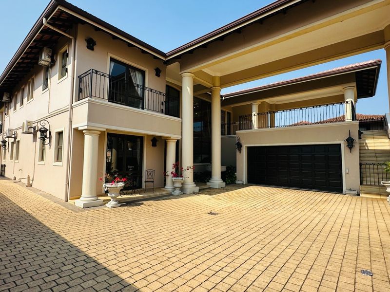 A well-maintained multi-story residential property featuring a paved driveway, double garage, and an upper-level balcony with decorative wrought iron railings.