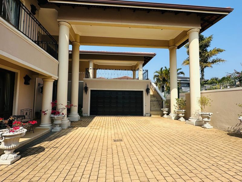Spacious paved driveway leading to a covered portico and garage, featuring elegant structural columns and wrought iron balcony detailing.