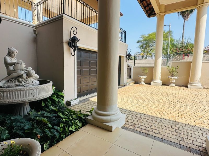 A spacious covered patio area featuring classic stone columns, paved flooring, and access to the garage, overlooking a private courtyard.