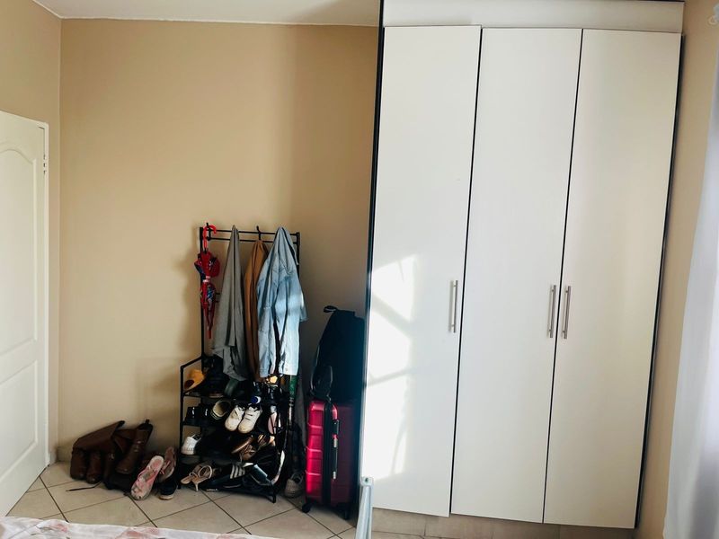A bedroom featuring a white built-in wardrobe with modern handles and neutral tiled flooring.
