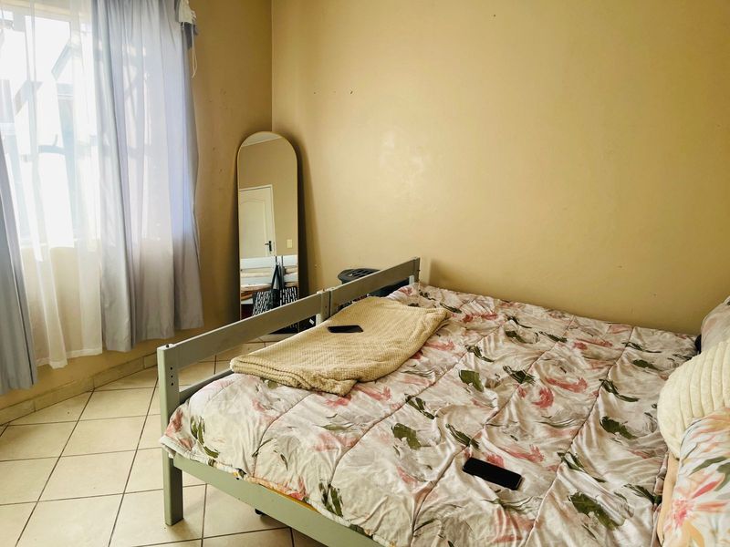 A bedroom featuring tiled flooring and a window, currently showing signs of wear on the wall surfaces.