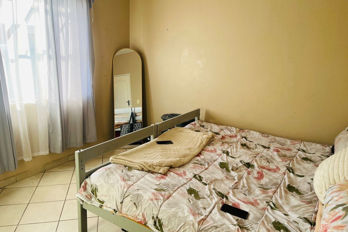 A bedroom featuring tiled flooring and a window, currently showing signs of wear on the wall surfaces.