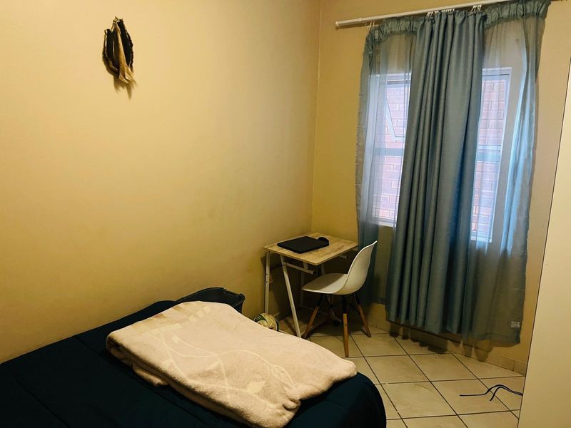 A compact bedroom featuring tiled flooring and a window with curtain fixtures, requiring minor wall repairs to improve the overall presentation.