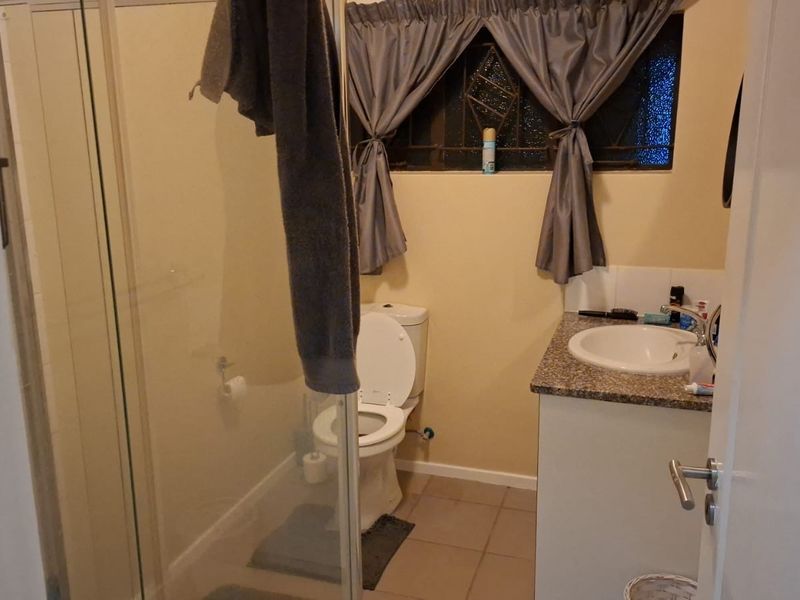 A functional bathroom featuring a glass shower enclosure, a toilet, and a vanity cabinet with a granite countertop.