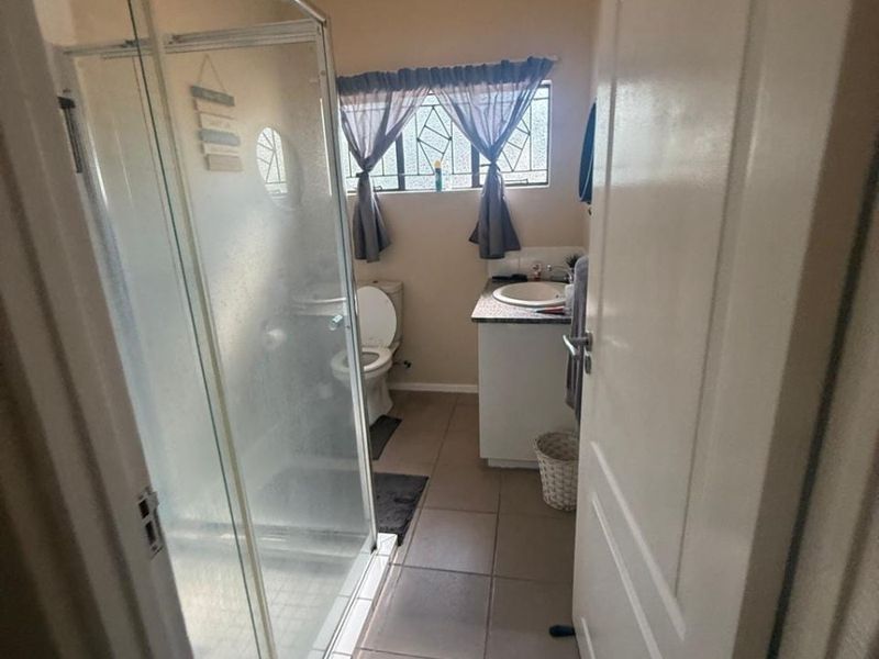 A functional bathroom featuring a glass shower enclosure, a vanity with a basin, and tiled flooring, illuminated by a central ceiling light.