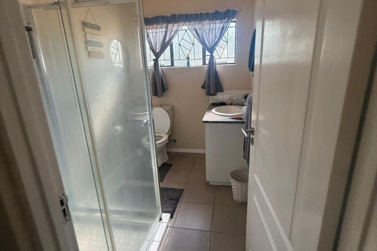 A functional bathroom featuring a glass shower enclosure, a vanity with a basin, and tiled flooring, illuminated by a central ceiling light.