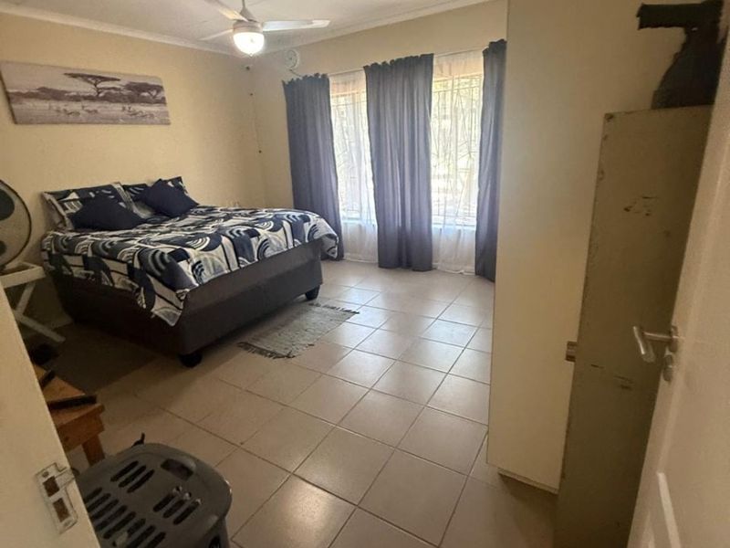 A functional bedroom featuring tiled flooring, a ceiling fan, and large windows fitted with security bars.
