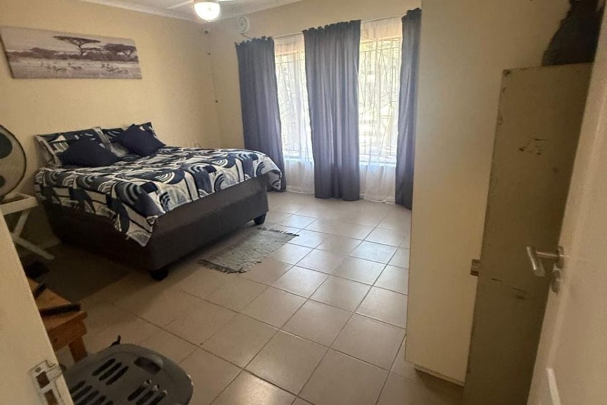 A functional bedroom featuring tiled flooring, a ceiling fan, and large windows fitted with security bars.