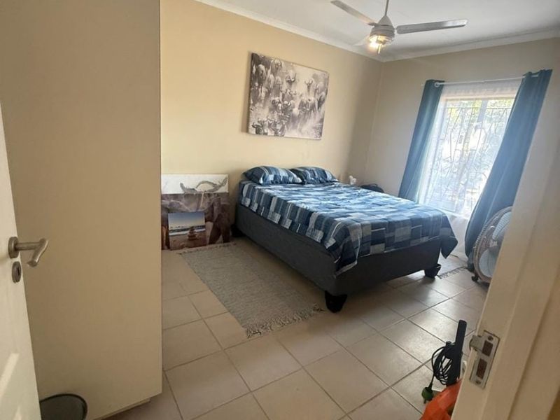 A functional bedroom featuring tiled flooring, a ceiling fan, and a security gate on the window, providing a simple and practical living space.