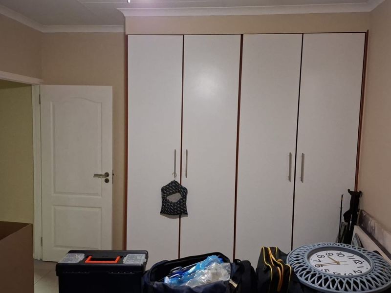 A bedroom featuring white built-in cupboards with modern handles and neutral wall finishes.
