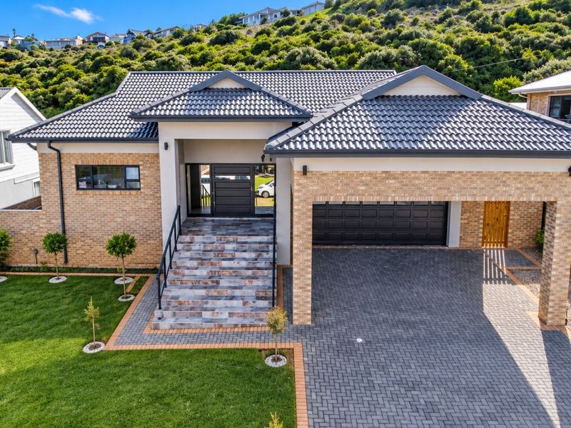 Modern single-story brick home featuring a tiled roof, double garage, paved driveway, and elevated entrance with tiled steps and landscaped front garden.