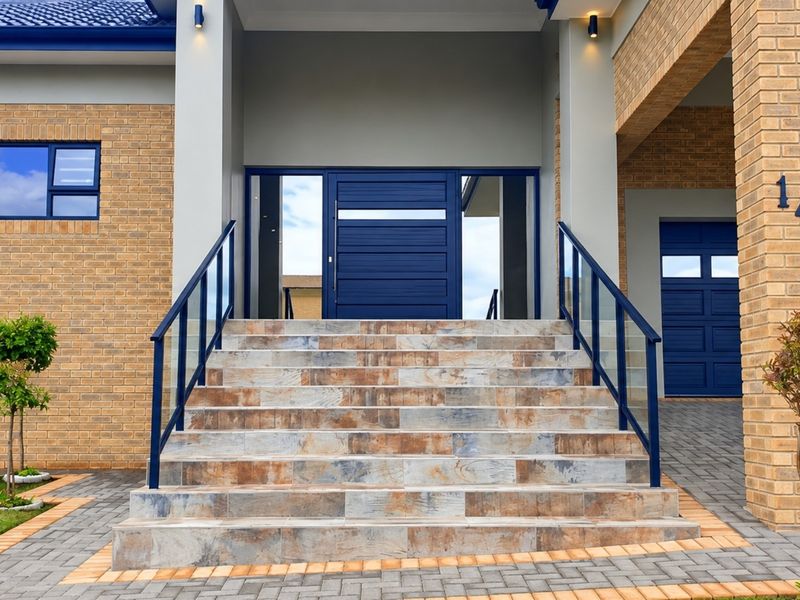 Modern front entrance featuring a tiled staircase with glass balustrades, face brick facade, and a striking blue front door with adjacent double garage.