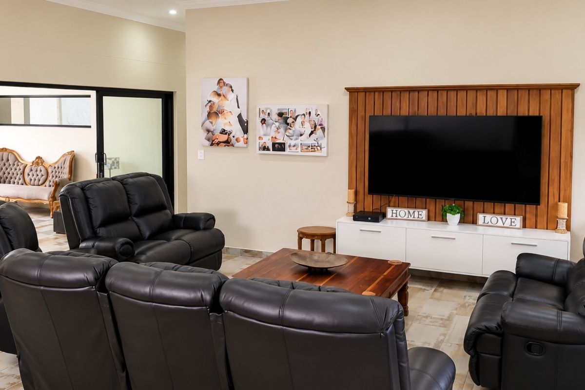 A comfortable living room featuring a prominent built-in wooden TV wall panel, tiled flooring, and access to an adjacent room through a sliding glass door.