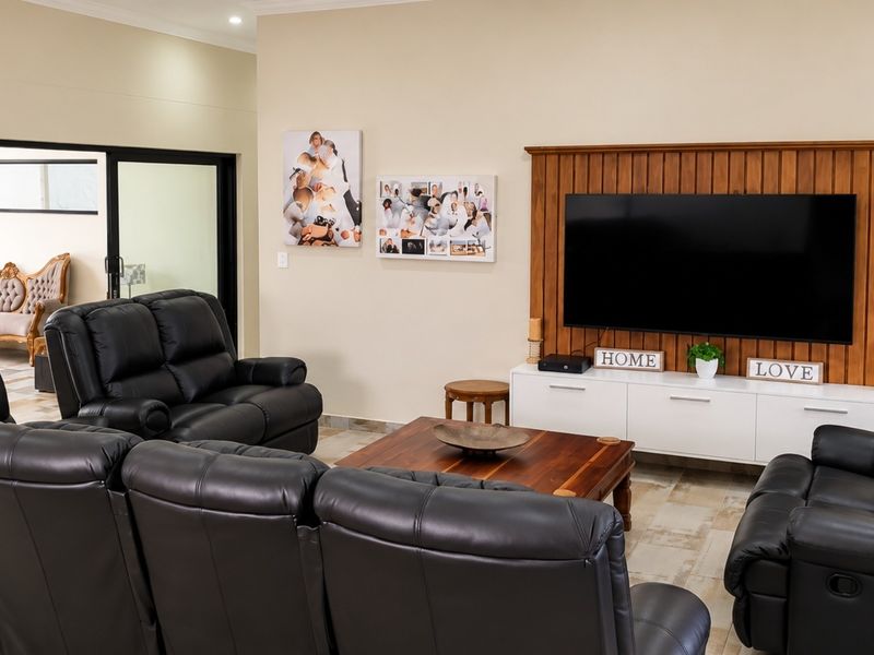 A comfortable living room featuring a prominent built-in wooden TV wall panel, tiled flooring, and access to an adjacent room through a sliding glass door.