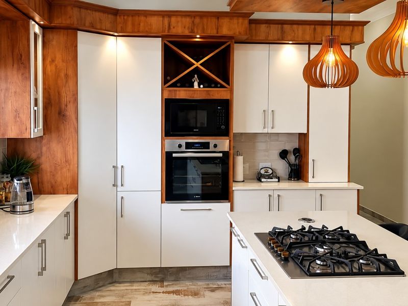 Modern kitchen featuring white cabinetry with wood accents, quartz countertops, a central island with a gas hob, and integrated built-in appliances.
