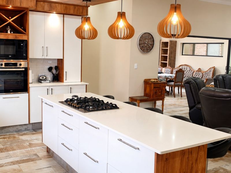 Modern open-plan kitchen featuring a central island with gas cooktop, built-in appliances, and stylish pendant lighting, seamlessly flowing into the adjacent living and dining areas.