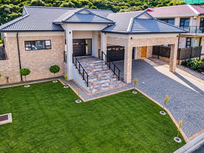 Modern single-story brick home featuring a tiled roof, paved driveway, double garage, and an elevated entrance with stone-clad stairs and manicured lawn.