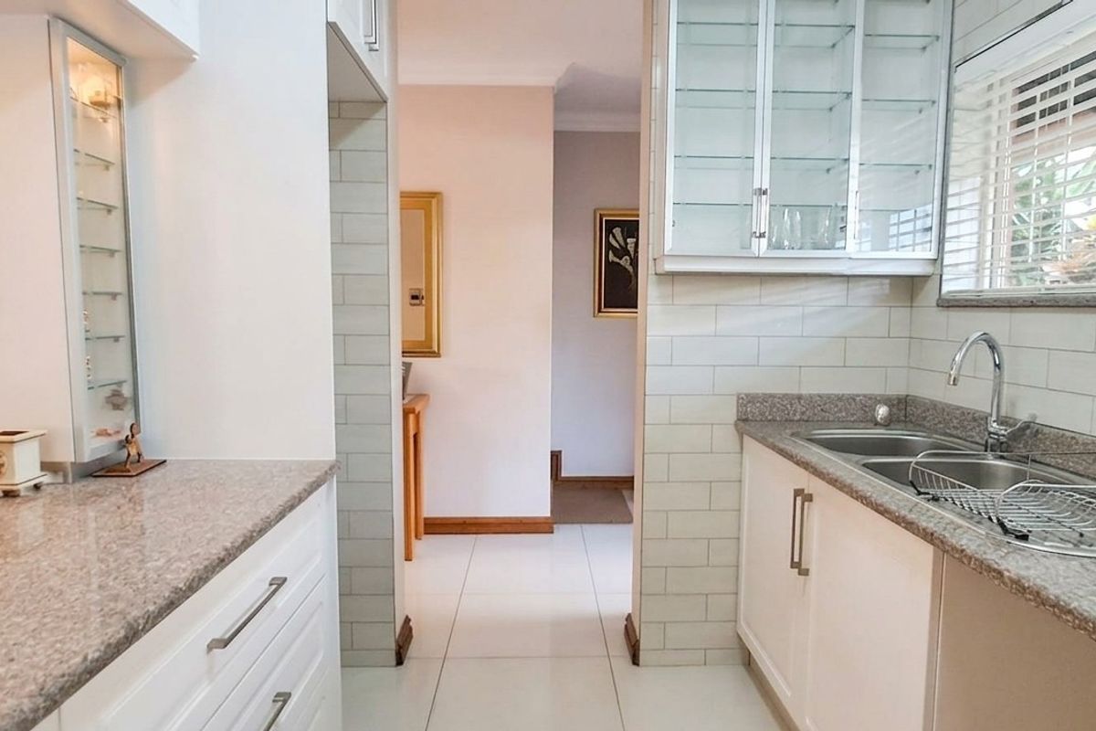A well-maintained kitchen featuring granite countertops, subway tile backsplash, and ample cabinetry, leading into a bright hallway.