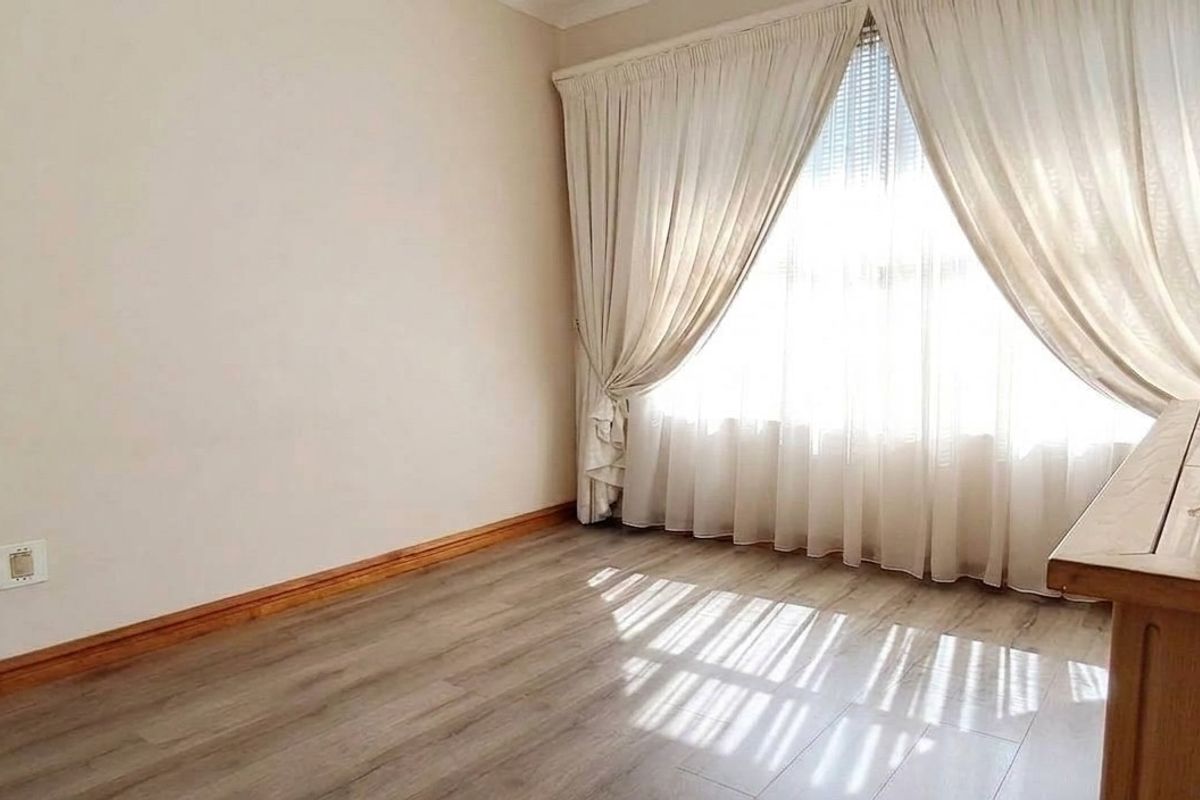 A bright bedroom featuring modern laminate flooring, neutral walls, and floor-to-ceiling curtains, offering a clean and comfortable living space.