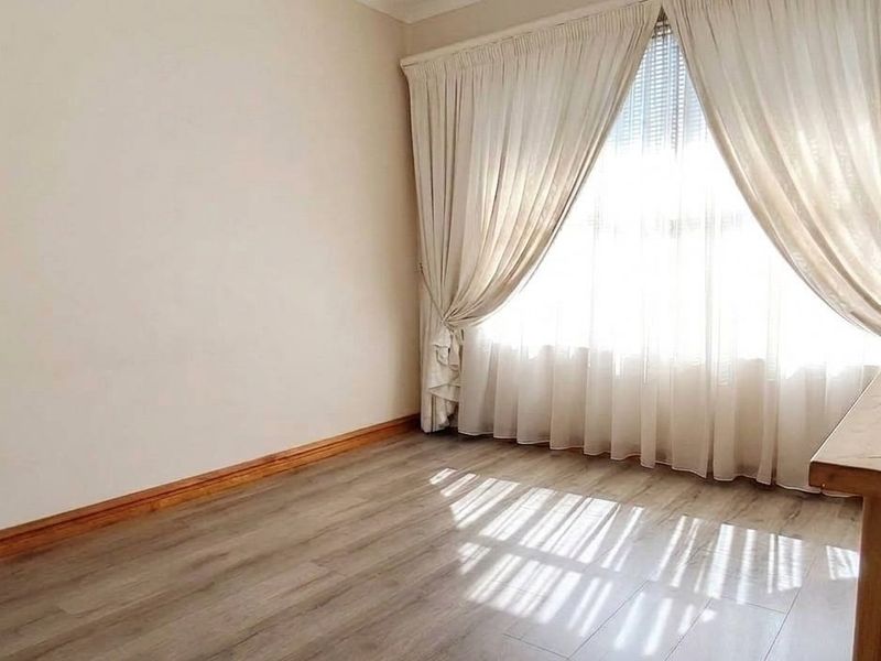 A bright bedroom featuring modern laminate flooring, neutral walls, and floor-to-ceiling curtains, offering a clean and comfortable living space.