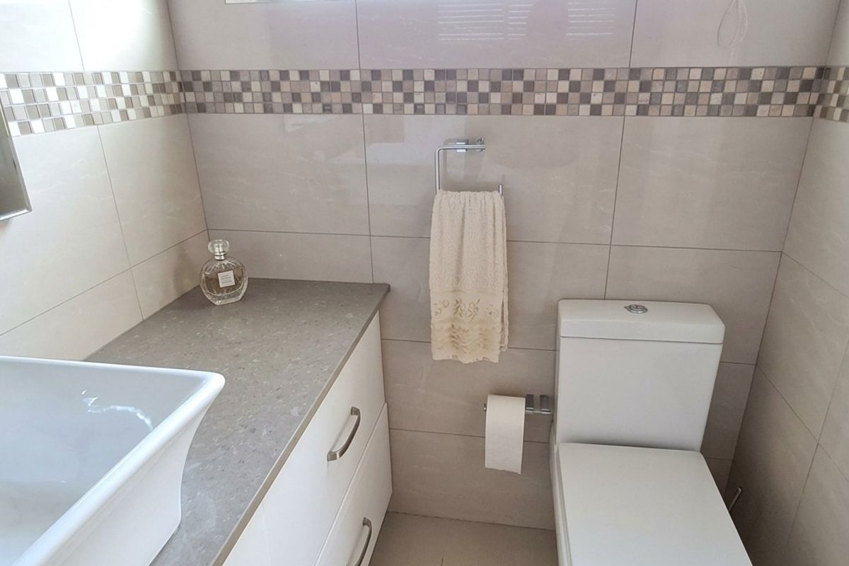 A modern bathroom featuring a vessel sink on a stone-topped vanity cabinet, a wall-mounted mirror, and neutral wall tiling with a decorative mosaic border.