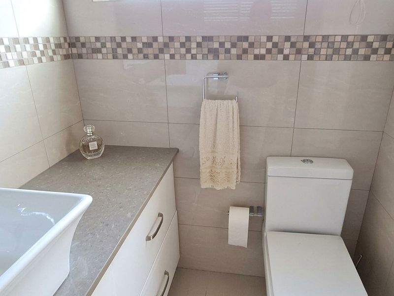 A modern bathroom featuring a vessel sink on a stone-topped vanity cabinet, a wall-mounted mirror, and neutral wall tiling with a decorative mosaic border.