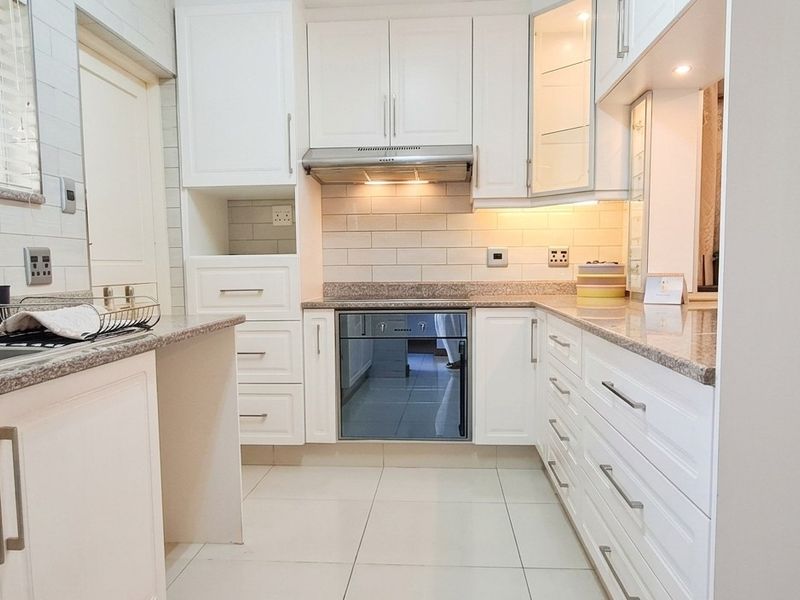 A clean, modern kitchen featuring white shaker cabinetry, granite countertops, subway tile backsplash, and integrated stainless steel appliances with ample storage space.