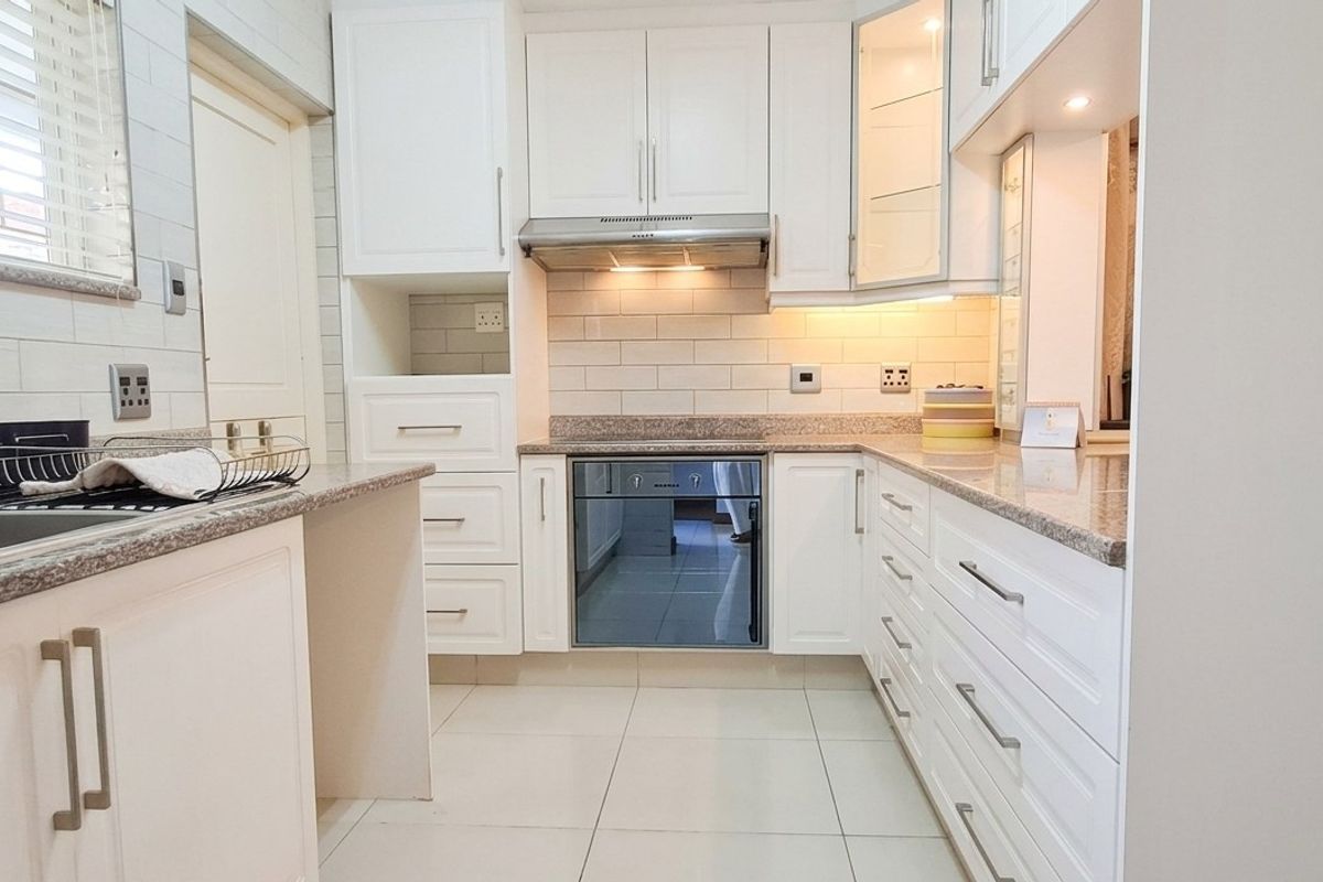 A clean, modern kitchen featuring white shaker cabinetry, granite countertops, subway tile backsplash, and integrated stainless steel appliances with ample storage space.