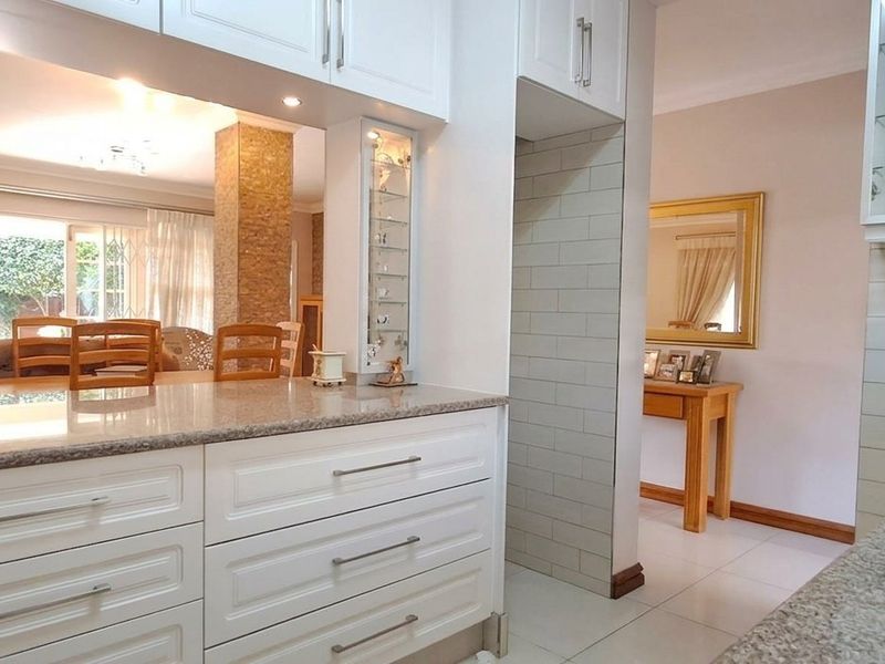 Open-plan kitchen featuring white cabinetry, granite countertops, and a subway tile backsplash, flowing seamlessly into the adjacent dining area with a stone-clad feature pillar.
