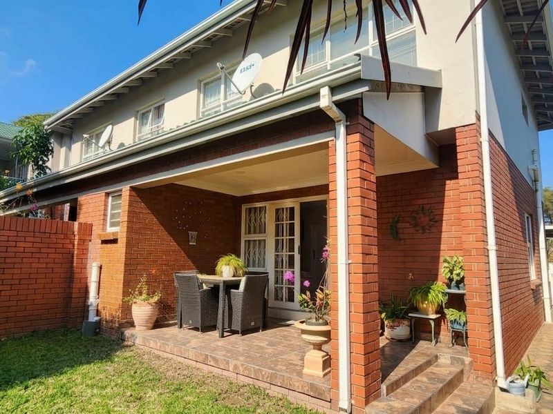 Rear view of the townhouse featuring a covered brick patio, tiled flooring, and a private garden area with brick boundary walls.