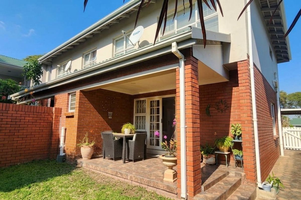 Rear view of the townhouse featuring a covered brick patio, tiled flooring, and a private garden area with brick boundary walls.
