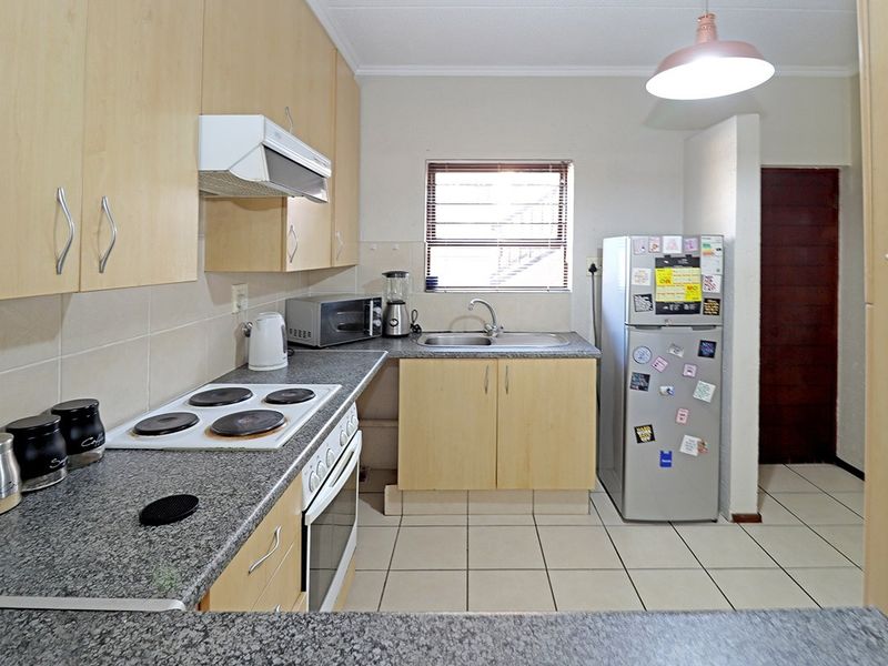 Functional kitchen featuring laminate cabinetry, granite countertops, built-in electric hob and oven, extractor fan, and tiled flooring.