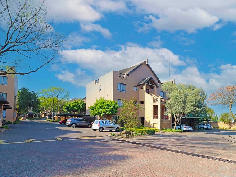 Exterior view of a multi-story apartment complex featuring paved driveway access and covered parking facilities.