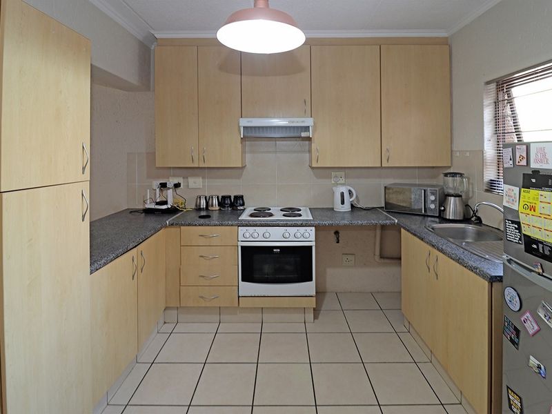 A functional U-shaped kitchen featuring light wood-tone cabinetry, granite-look laminate countertops, an electric stove with extractor, and tiled flooring.