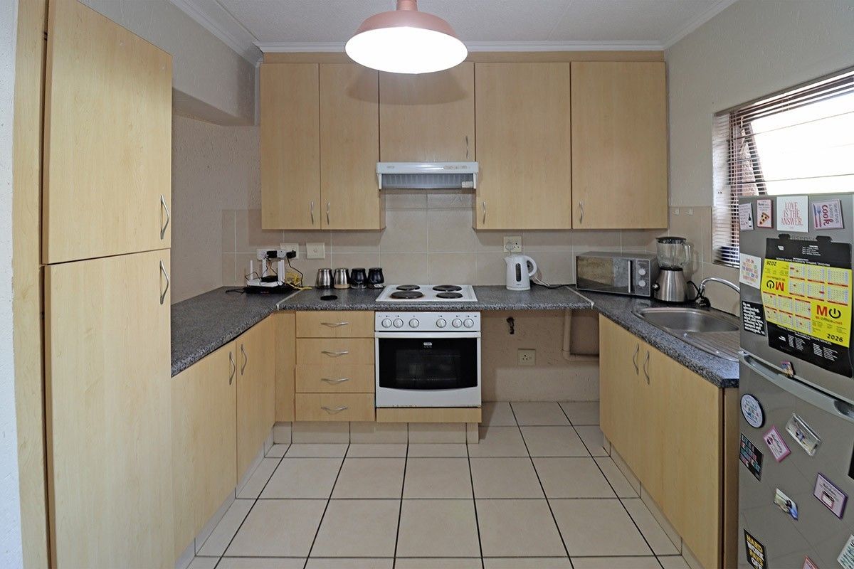 A functional U-shaped kitchen featuring light wood-tone cabinetry, granite-look laminate countertops, an electric stove with extractor, and tiled flooring.