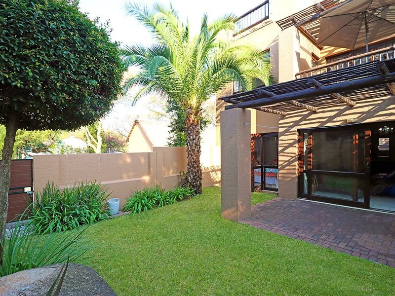 A private rear garden featuring a paved patio area with a timber pergola, established landscaping, and direct access to the apartment via sliding doors.