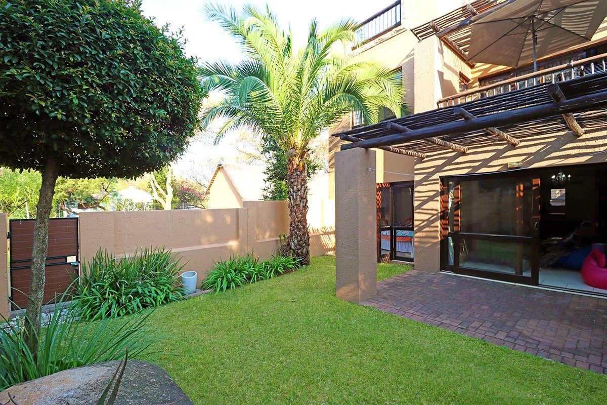 A private rear garden featuring a paved patio area with a timber pergola, established landscaping, and direct access to the apartment via sliding doors.