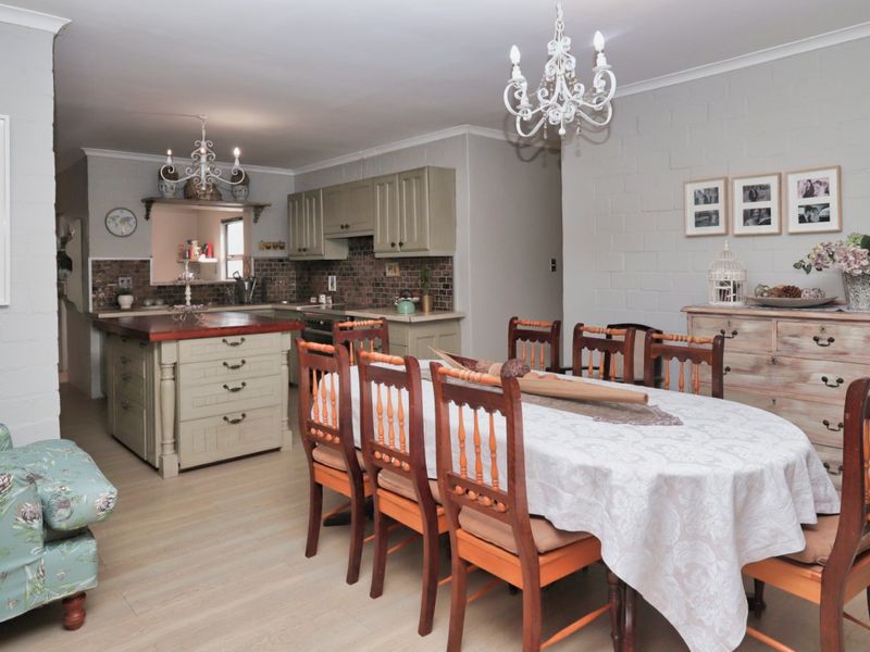 Open plan kitchen and dining area featuring a central island, tiled backsplash, and neutral painted brick walls with classic light fixtures.