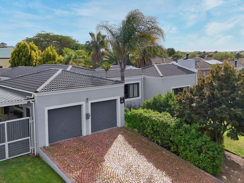 Aerial view of the front elevation featuring a double garage, brick paved driveway, and well-maintained tiled roof structure.