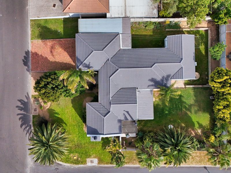 Aerial view of the property showcasing the tiled roof, surrounding landscaped garden, swimming pool, and paved driveway area.